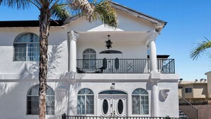 Un edificio de dos pisos con balcón, ventanas arqueadas y fachada blanca.