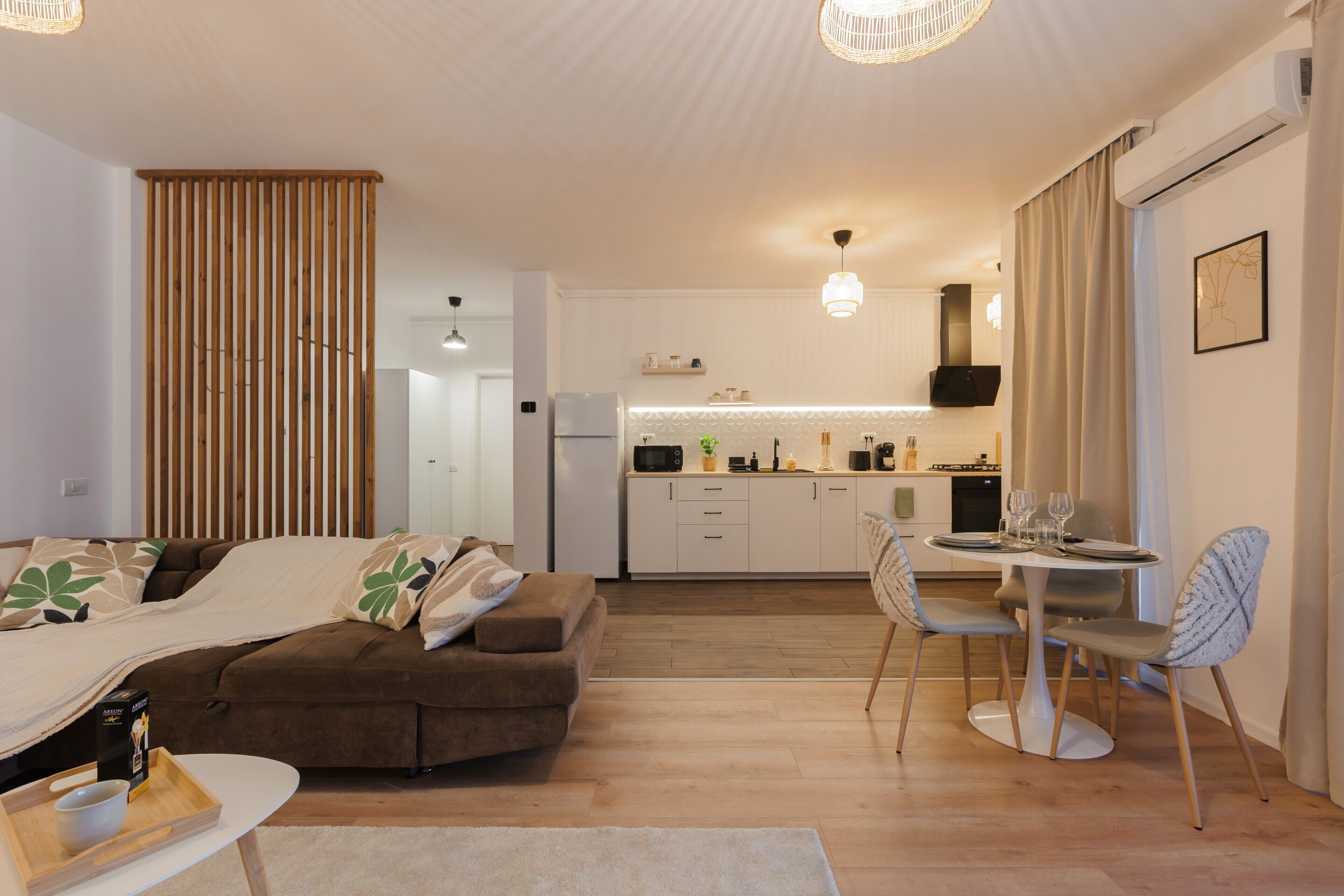 A modern hotel room with a sofa, dining table, and kitchen area.