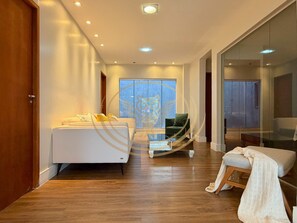 A modern hotel room with a bed, a seating area, and a large window.