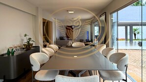 Un espace repas moderne avec une longue table, six chaises et un canapé de couleur sombre.
