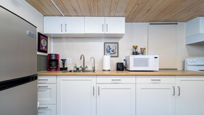 A kitchen with white cabinets, a wooden countertop, a coffee maker, a microwave, and a sink.