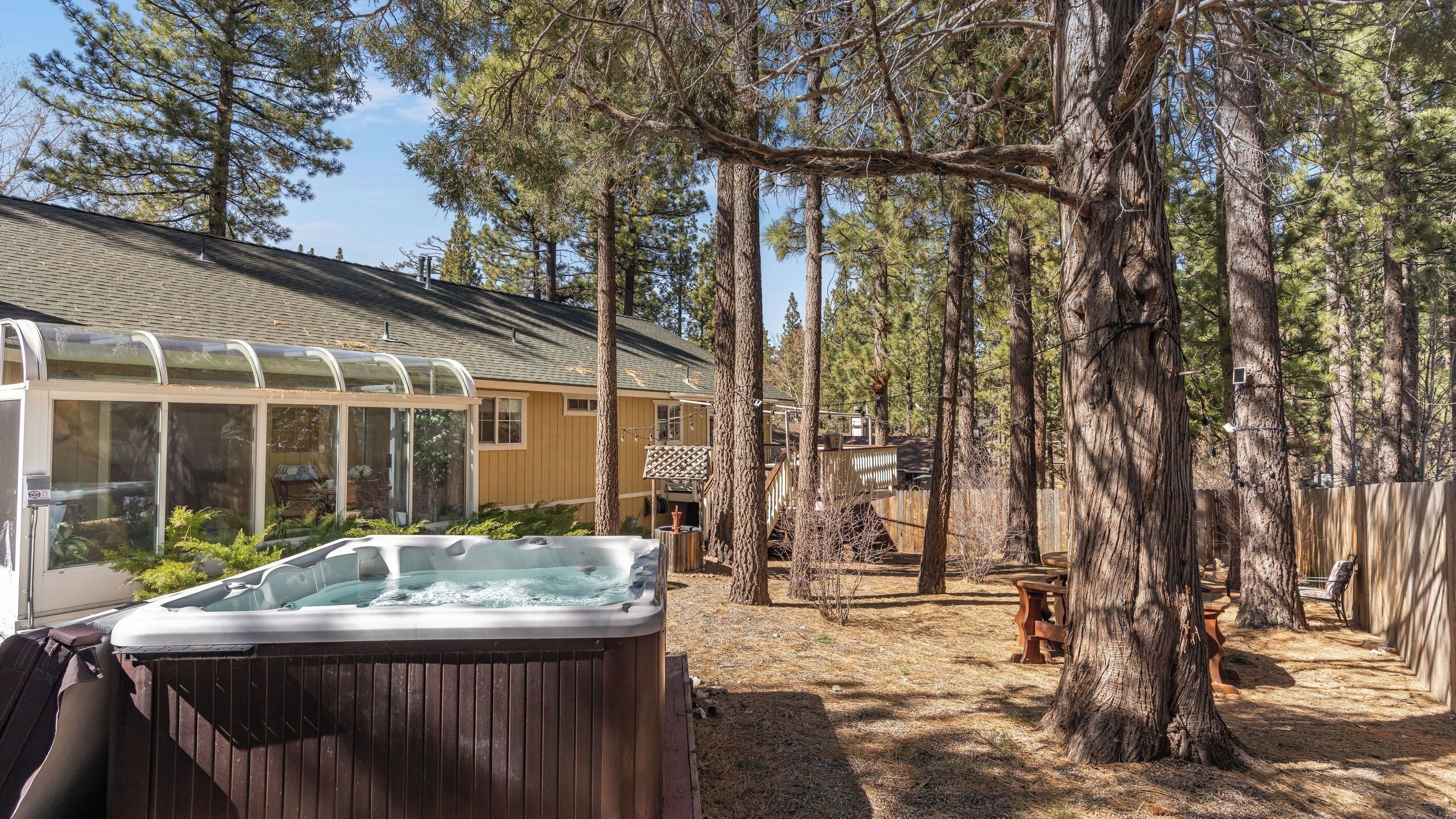 A hot tub in a wooded backyard with a glass-enclosed patio and a wooden deck.