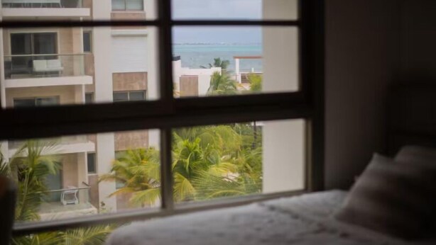 Ein Zimmer mit großem Fenster, einem Bett und Blick auf ein Gebäude sowie Palmen.