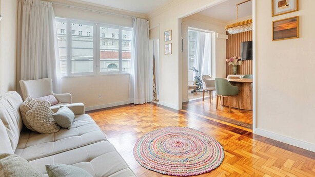 Een woonkamer met een bank, een kleurrijk vloerkleed, een eethoek met stoelen en een televisie aan de muur.