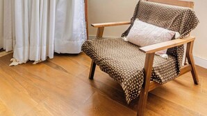 Een kamer met een houten stoel, een raam met uitzicht op gebouwen en een gordijn.