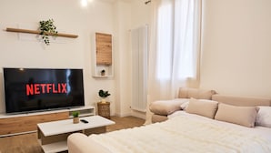 A modern bedroom with a large bed, a TV displaying 'NETFLIX,' a wooden shelf, and a radiator. - Ortensie House (Padua)