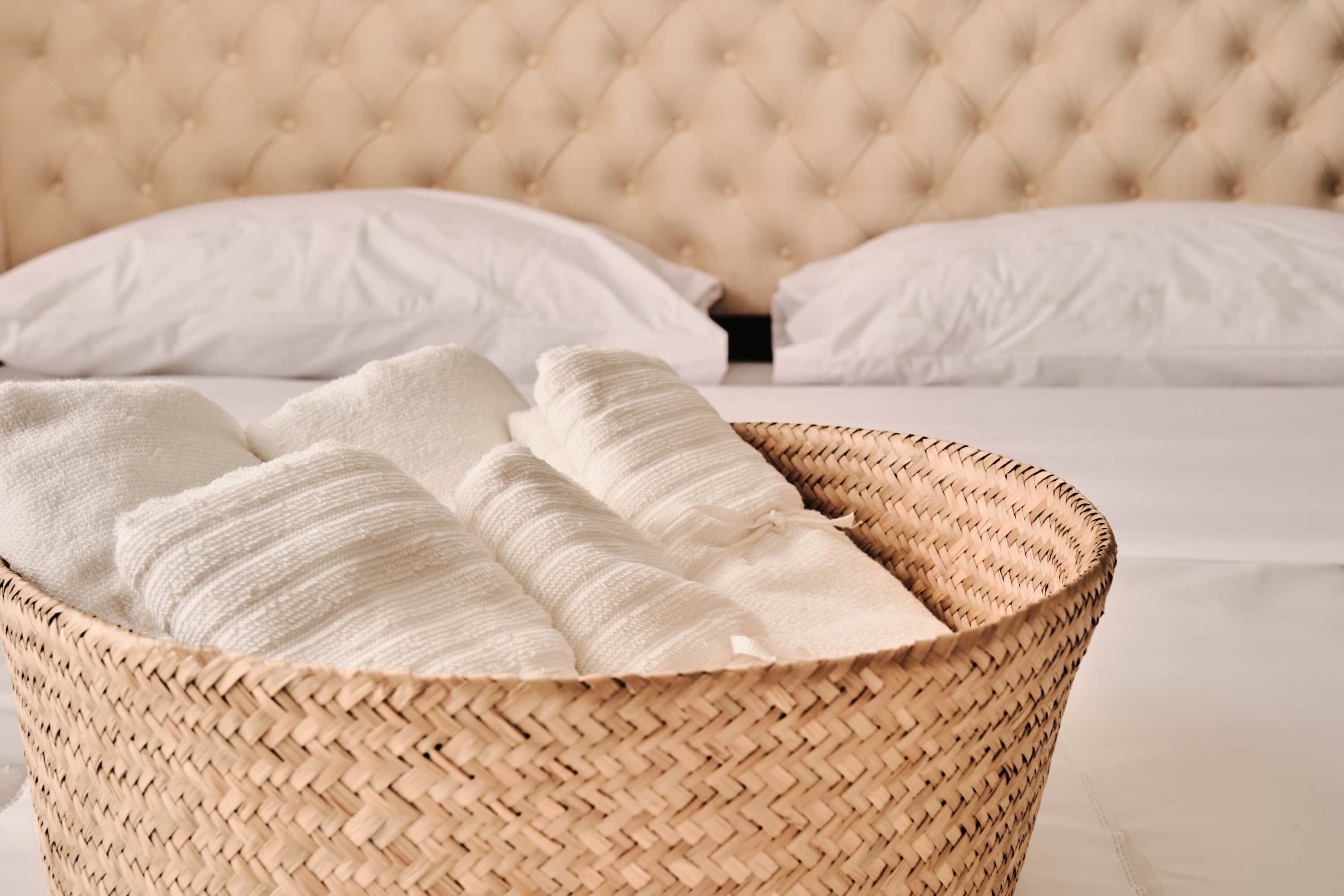 Ein Bett mit einem gesteppten Kopfteil, weißen Kissen und einem gewebten Korb mit gefalteten Handtüchern.