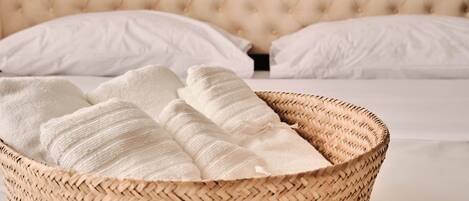 A bed with a tufted headboard, white pillows, and a woven basket with folded towels.