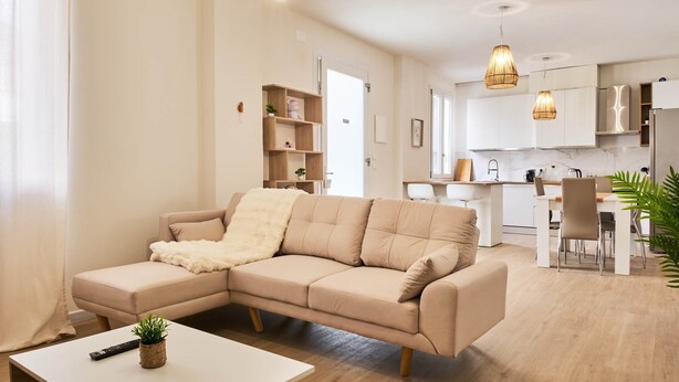 A modern living room with a beige sectional sofa, a white coffee table, and a kitchen area in the background. - Ortensie House (Padua)