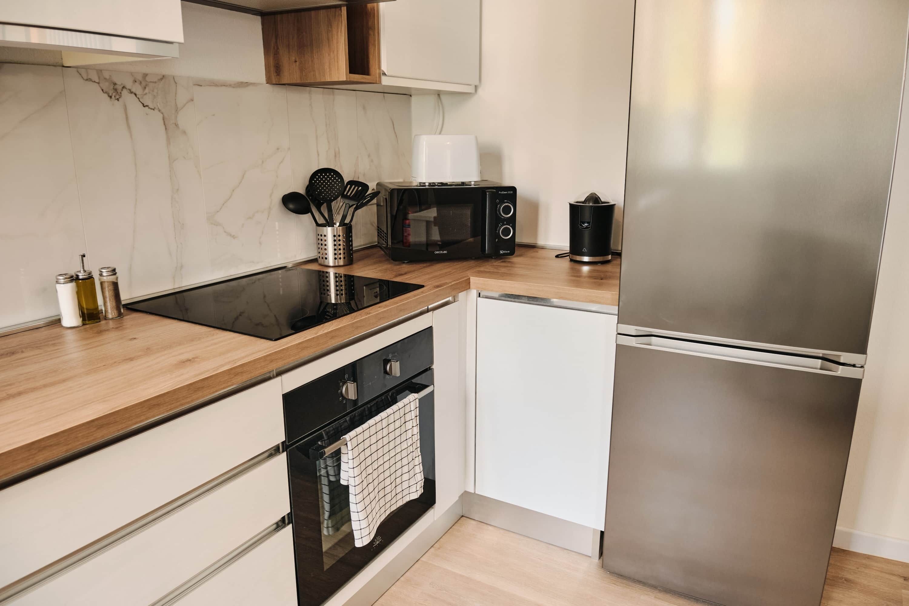 Una cucina moderna con un piano cottura a induzione nero, un forno a microonde, un frigorifero in acciaio inossidabile e mobili bianchi.