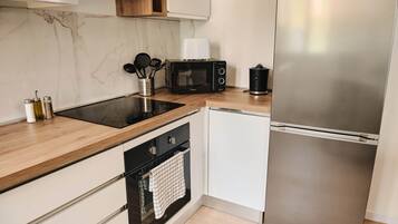 Una cucina moderna con un piano cottura a induzione nero, un forno a microonde, un frigorifero in acciaio inossidabile e mobili bianchi.