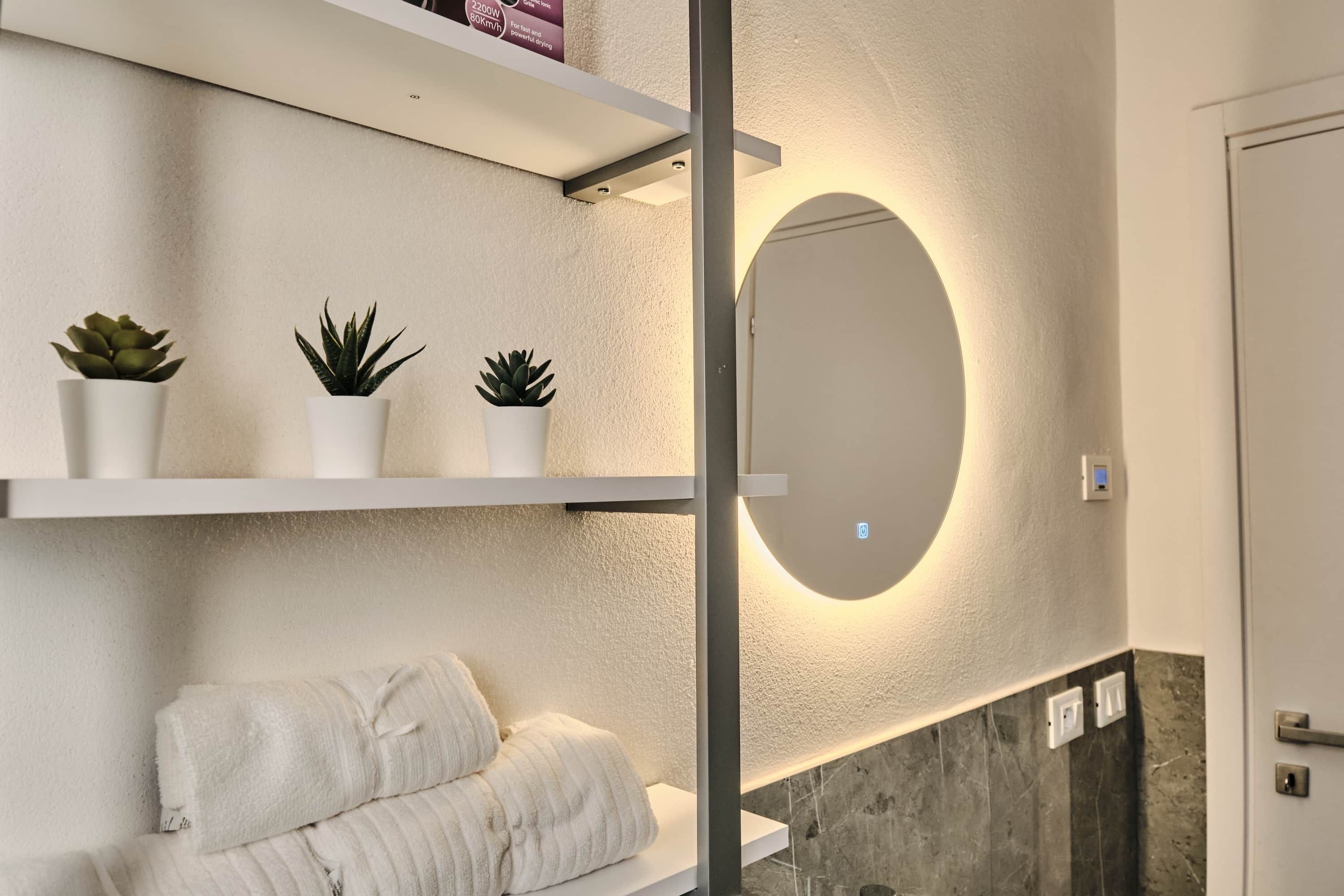 Un bagno moderno con uno specchio grande, scaffali bianchi con piante in vaso e un porta asciugamani.