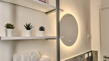 Un bagno moderno con uno specchio grande, scaffali bianchi con piante in vaso e un porta asciugamani.