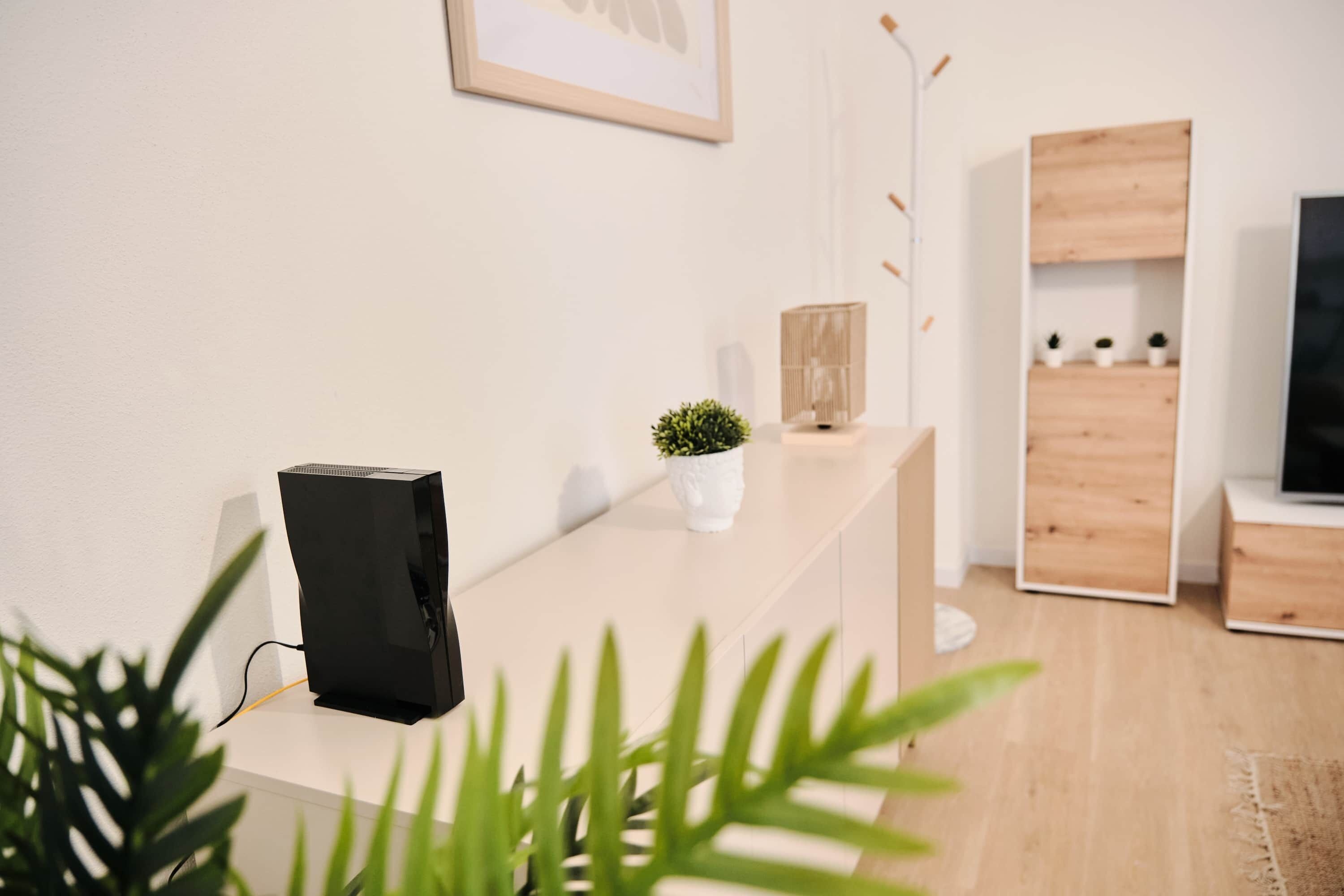 Quarto moderno com uma escrivaninha branca, um alto-falante preto, uma pequena planta em vaso e um armário de madeira com prateleiras.