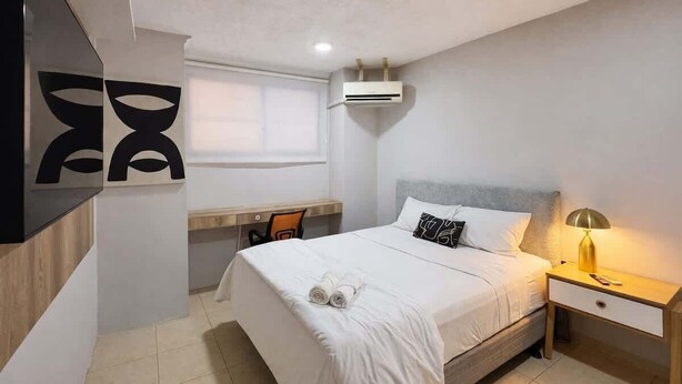 A hotel room with a bed, a desk, a chair, a lamp, and an air conditioning unit. - Suite at Lomas de Urdesa walk to Tennis Federation (Guayaquil)