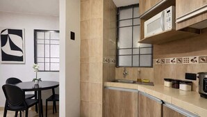 A compact kitchen with a microwave, sink, and cabinets. There's a dining table with chairs and a small trash bin. - Suite at Lomas de Urdesa walk to Tennis Federation (Guayaquil)