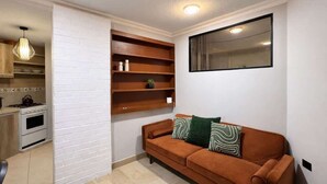 A living room with a sofa, a wall-mounted TV, and a kitchen area with a stove and cabinets. - Suite at Lomas de Urdesa walk to Tennis Federation (Guayaquil)