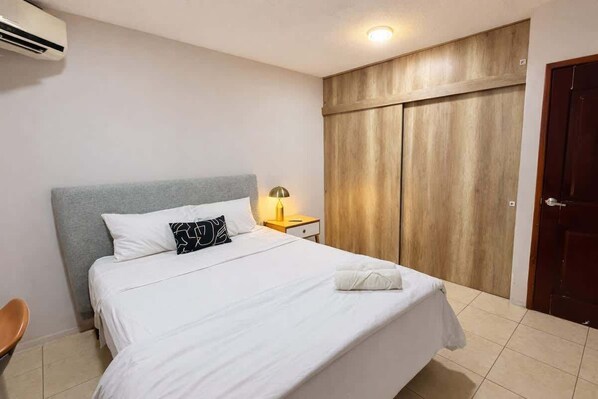 A hotel room with a bed, a nightstand with a lamp, a wardrobe, and a door.