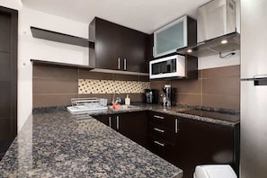 A modern kitchen with dark cabinetry, a granite countertop, a microwave, and a coffee maker.