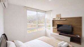 A hotel room with a bed, a TV, a window with a view, and a shelf with a sign. - Elegant Apartment free parking near US Consulate (Guayaquil)