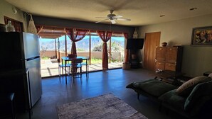 Una sala de estar con comedor, un ventilador de techo, un televisor de pantalla plana y vistas a montañas a través de ventanas amplias.