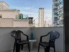 Ein Balkon mit zwei schwarzen Plastikstühlen, einem kleinen weißen Tisch und einer blauen Wasserflasche.