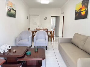 A living room with a sofa, two armchairs, a wooden coffee table, and a dining area with a table and chairs.