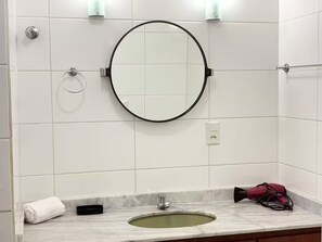 A bathroom with a round mirror, a sink, a towel, and a hairdryer.