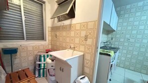 Eine kleine Küche mit Spüle, einem Kühlschrank und einem Fenster mit Jalousien.