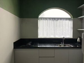 A kitchen with a black countertop, a sink, and a window with a white curtain. - 2 Bedrooms, Garage and Close to the Beach (Balneário Camboriú)
