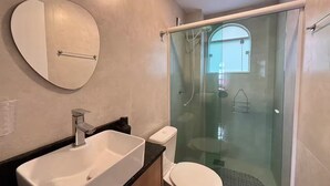 Un baño con un espejo grande, un lavamanos, un inodoro y una ducha con mampara de vidrio.