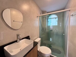 Une salle de bain avec un grand miroir, un lavabo, des toilettes et une douche à parois de verre.
