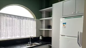 Una cocina con un lavamanos, una ventana con cortinas de encaje y un refrigerador blanco.