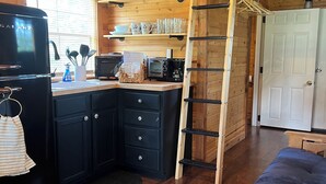 Ein gemütliches Blockhäuschen mit Küchenzeile, Schlafkoje und Holzbalkendecke.