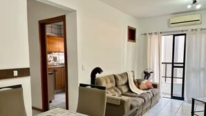 Een woonkamer met een bank, een eettafel en een keuken die zichtbaar is door een open doorgang.