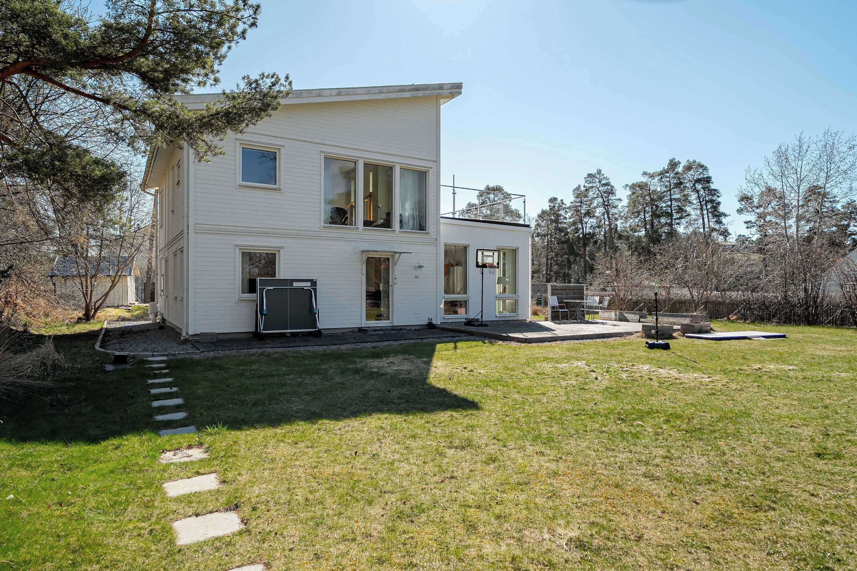 Une maison blanche à deux étages, avec un garage apparent, une allée pavée et une pelouse.