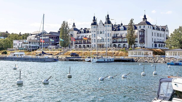 Un bâtiment situé au bord de l’eau, avec plusieurs étages, un quai où sont amarrés des bateaux et un ciel dégagé.
