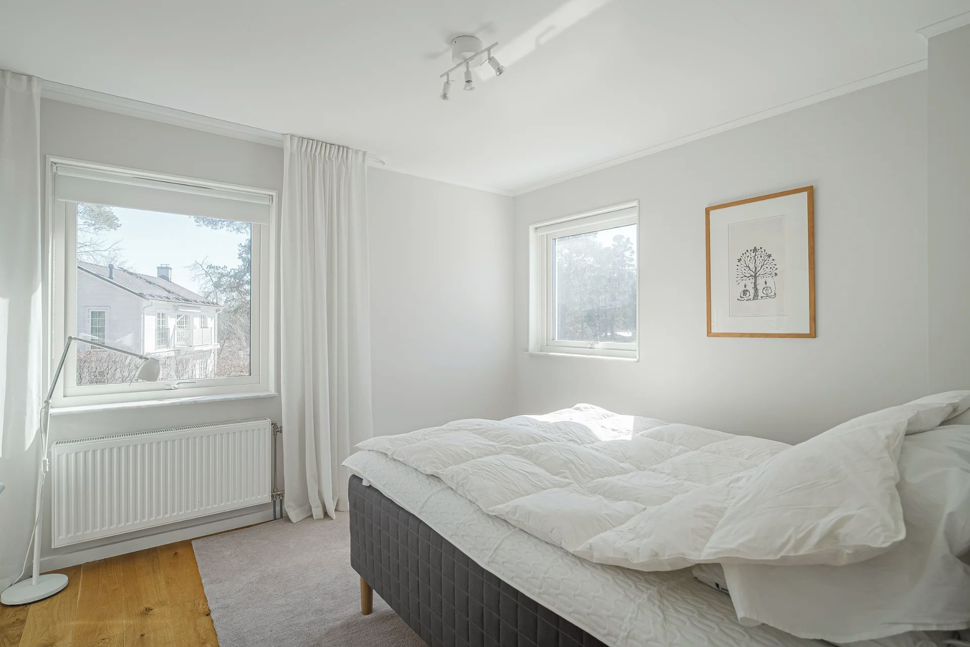 Et soveværelse med seng, to vinduer, en radiator og en loftslampe.