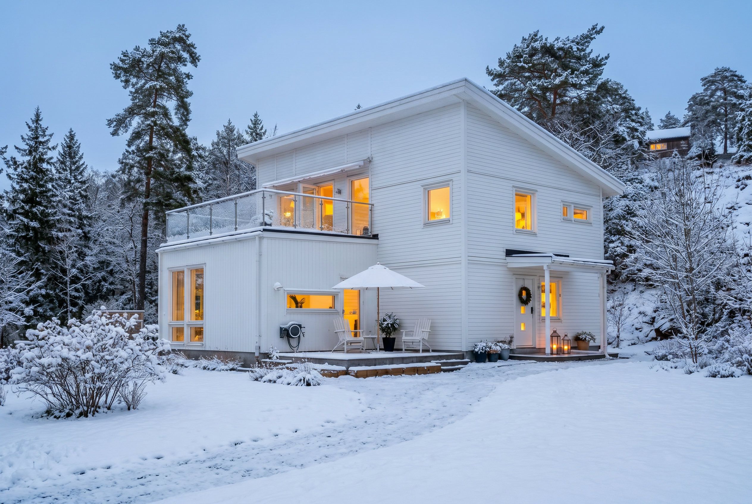 Een wit huis met twee verdiepingen, een balkon en een veranda, met een besneeerd landschap.