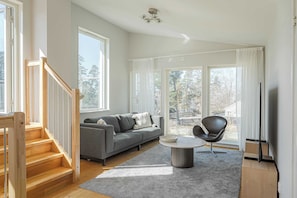 A modern living room with a staircase, a grey sofa, a round coffee table, and a black chair. - Lakefront Villa in Saltsjöbaden near Stockholm (Saltsjöbaden)