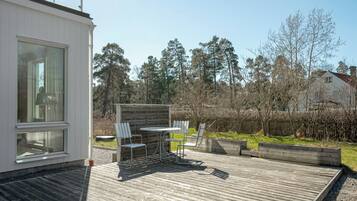 En moderne udendørs terrasse med et spisebord og stole, omgivet af et træhegn og træer.