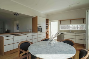 A modern kitchen with white cabinetry, a dining area with a marble table, and a view through a window. - Lakefront Villa in Saltsjöbaden near Stockholm (Saltsjöbaden)