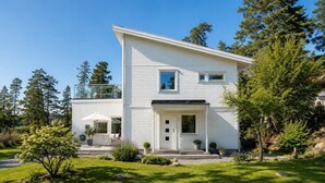 Une maison blanche à deux étages, dotée d’un balcon, d’un porche et d’une pelouse bien entretenue.