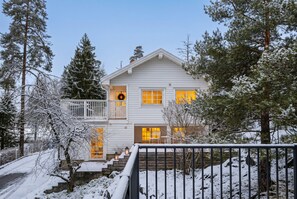 A two-story house with a balcony, a front porch with steps, and a snow-covered landscape.