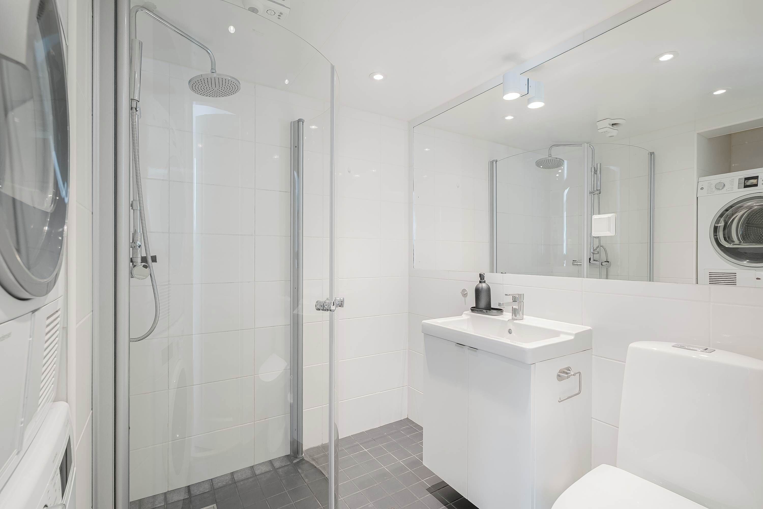 A modern bathroom with a glass-enclosed shower, a white sink, and a built-in washing machine.