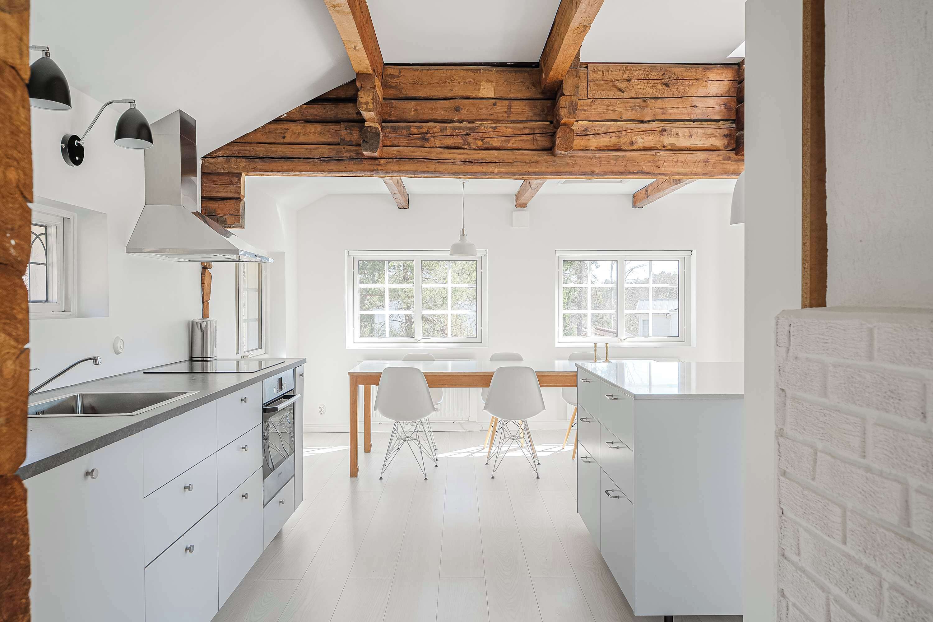 A modern kitchen with white cabinetry, a wooden ceiling, and a dining area with white chairs.