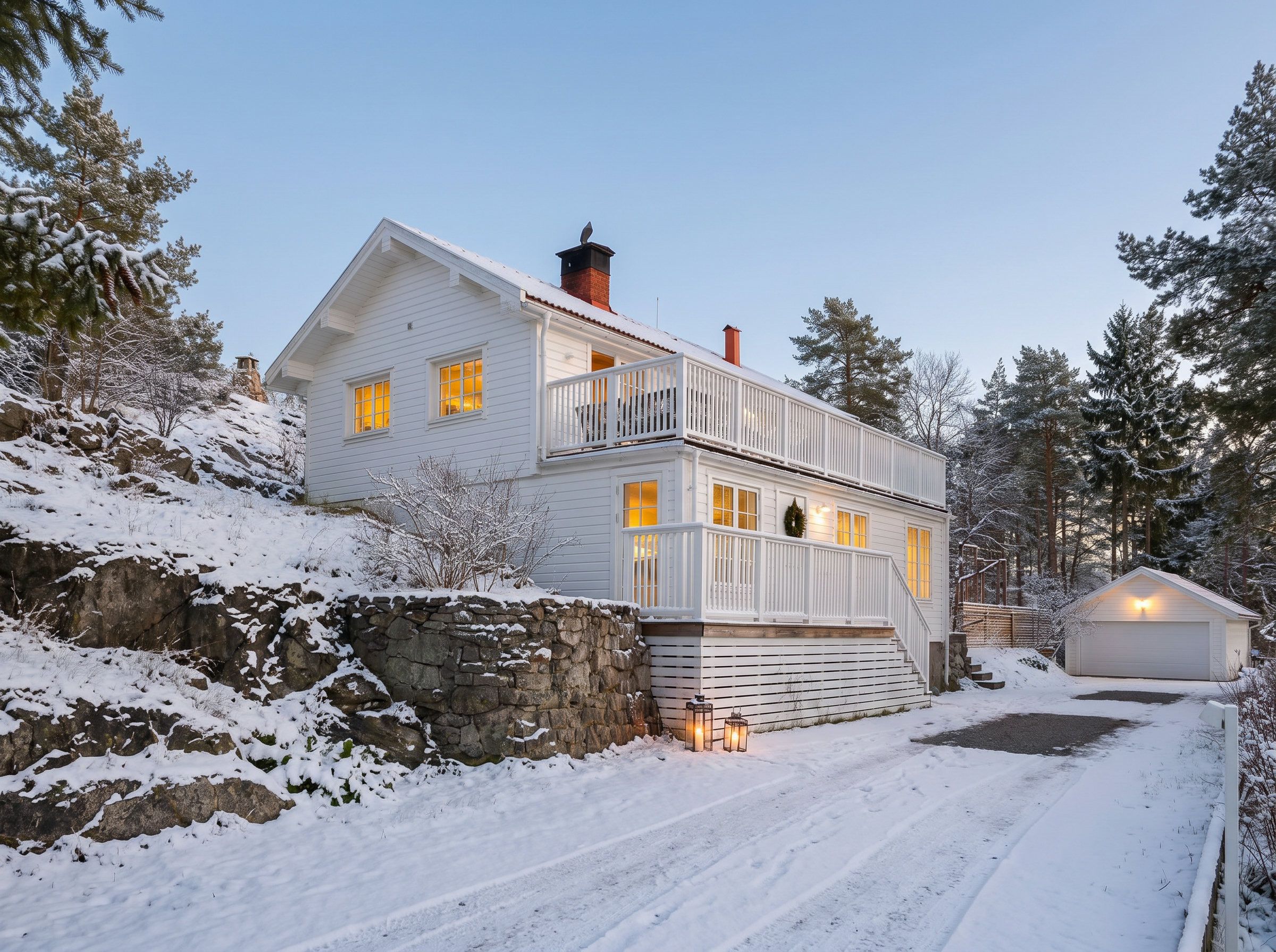 A two-story house with a stone wall, a garage, and a snow-covered driveway.