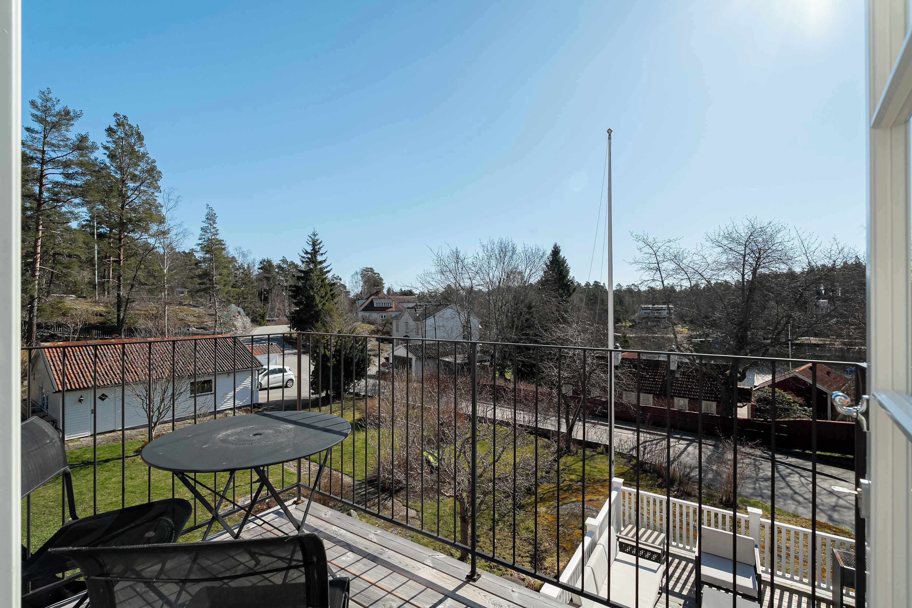 Un balcon avec une table et des chaises, une vue sur un quartier résidentiel et un ciel dégagé.