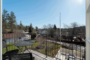 Un balcone con tavolo e sedie, vista su un quartiere residenziale e cielo sereno.