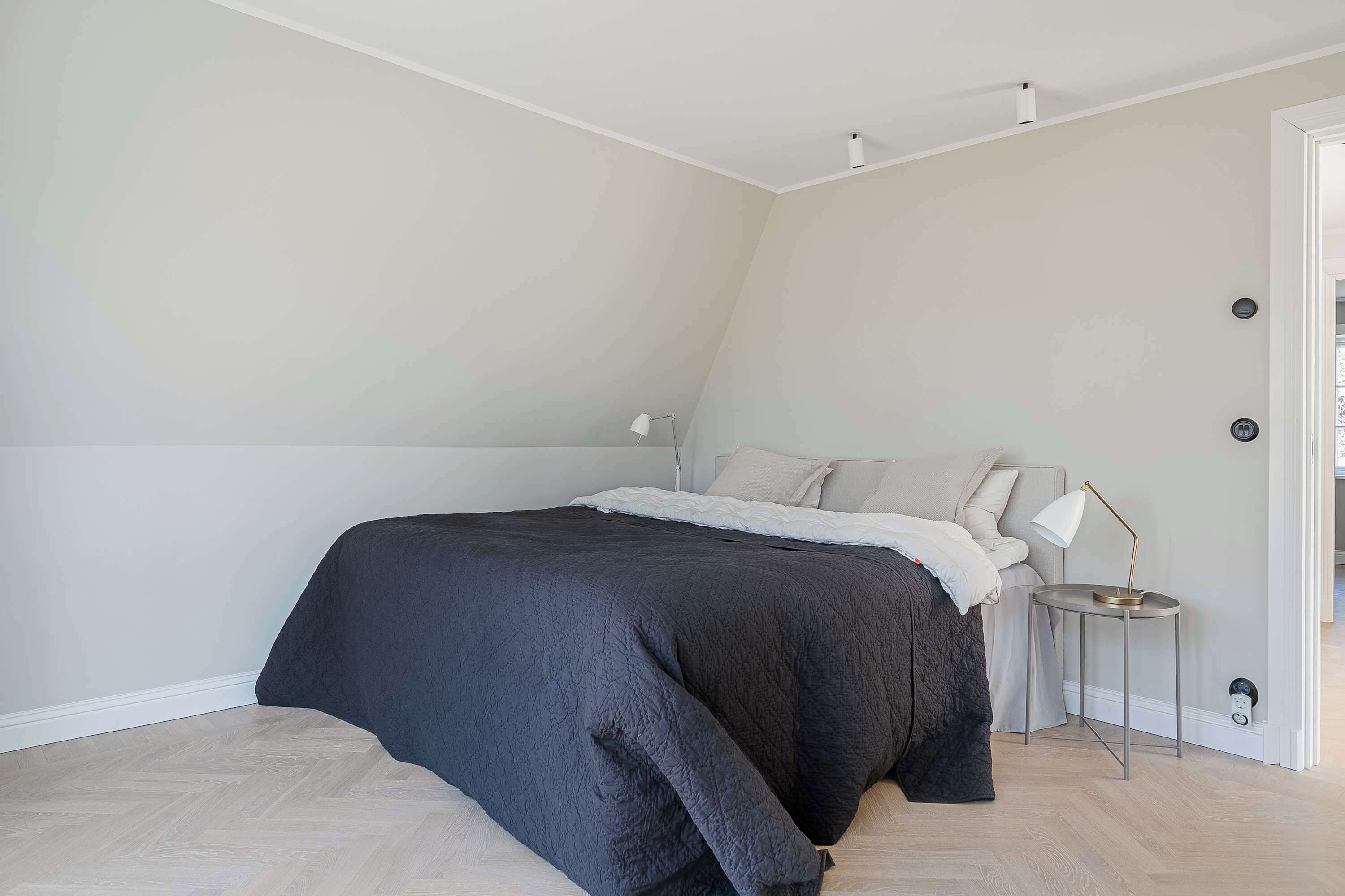 Een slaapkamer met een bed, nachtkastje en lamp.